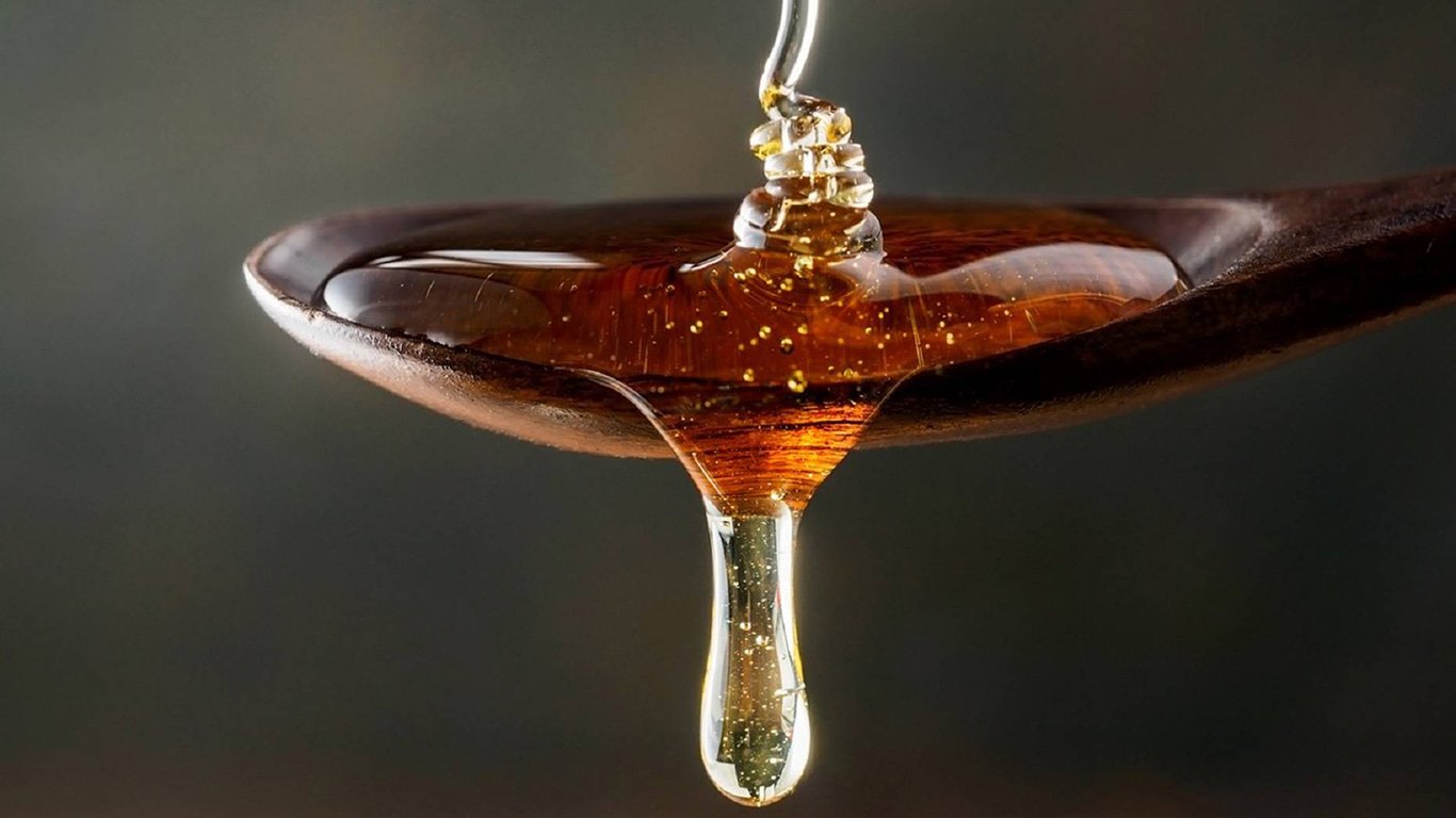 runny Manuka Honey dripping from a wooden spoon for blog: Can Manuka Honey stop me getting a virus?