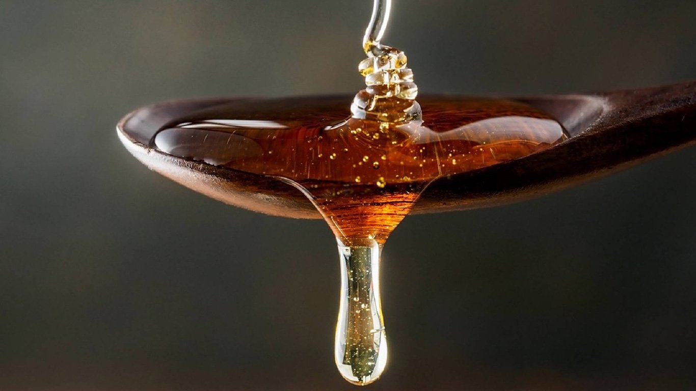 runny Manuka Honey dripping from a wooden spoon for blog: Can Manuka Honey stop me getting a virus? 