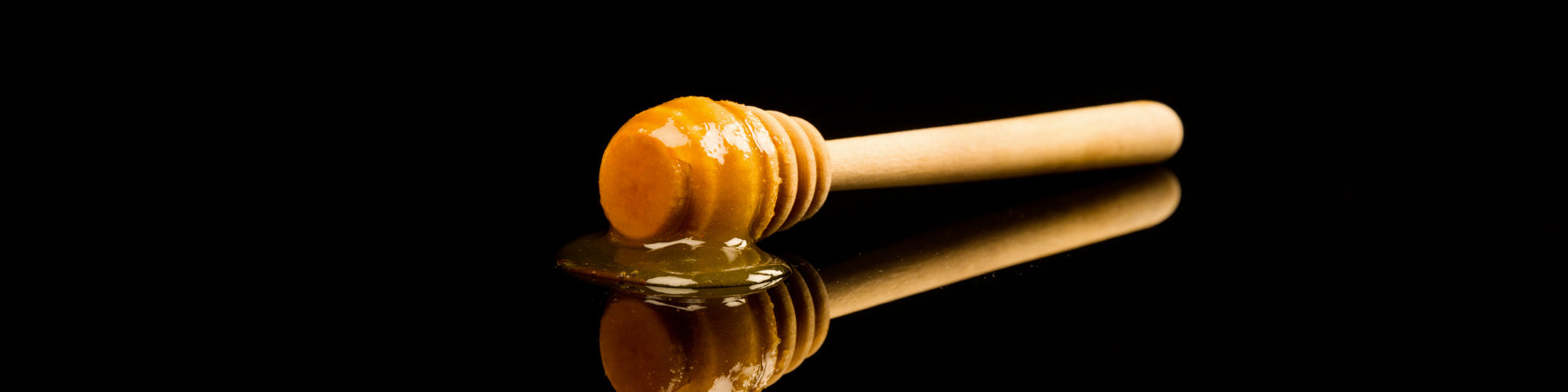Manuka Honey on a honey dipper on a black surface. 
