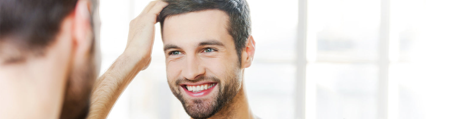Young handsome man admiring his mirror image and nice skin - used Manuka Honey mens skincare products