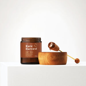 Jar of Rare Harvest honey with a wooden dipper on a white background