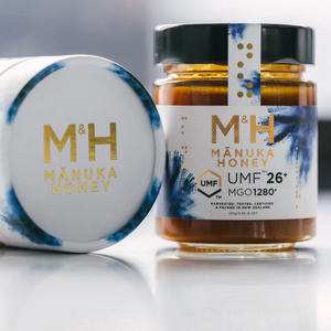 Two jars of M&H Manuka Honey on a reflective surface with a blurred background
