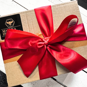 A square kraft paper gift box wrapped with a large shiny red satin ribbon bow and tied with a matching red ribbon, featuring a black brand label on the top left.