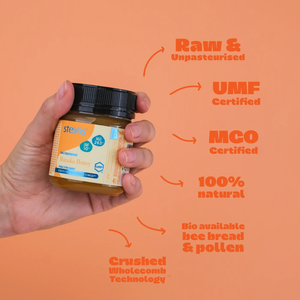 Hand holding a jar of honey with certification text on an orange background