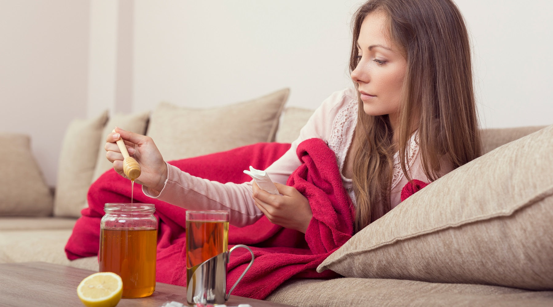 Woman feeling sick lying on the couch with Manuka honey tonic - strengthening the immune system is one of the benefits of Manuka Honey