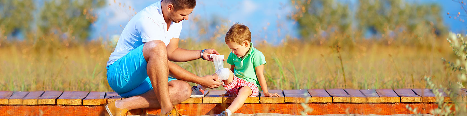 Father outdoors dressing son's knee with Manuka Honey First Aid dressing to treat burns, healing skin ulcers, and preventing scars
