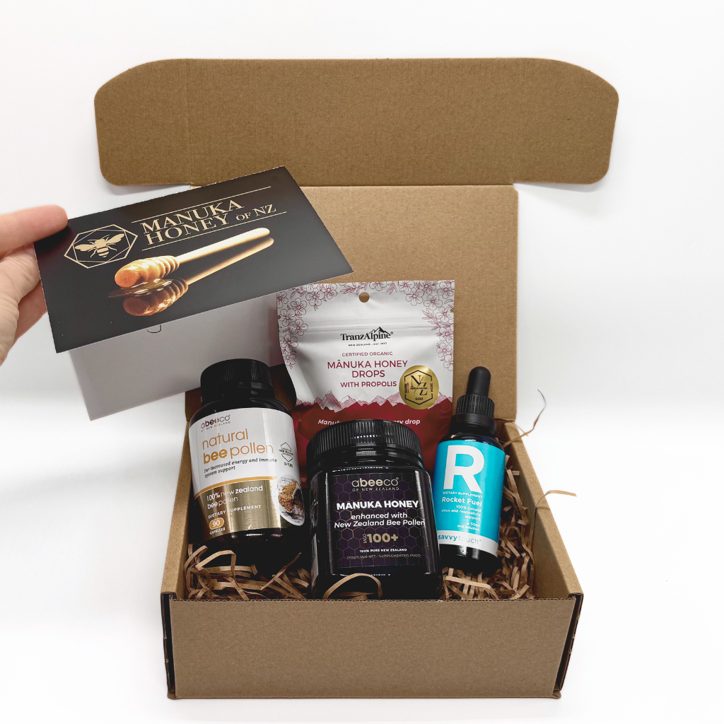 Open cardboard box containing Manuka honey products with a hand holding a card.