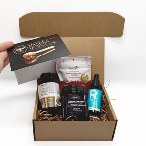Open cardboard box containing Manuka honey products with a hand holding a card.