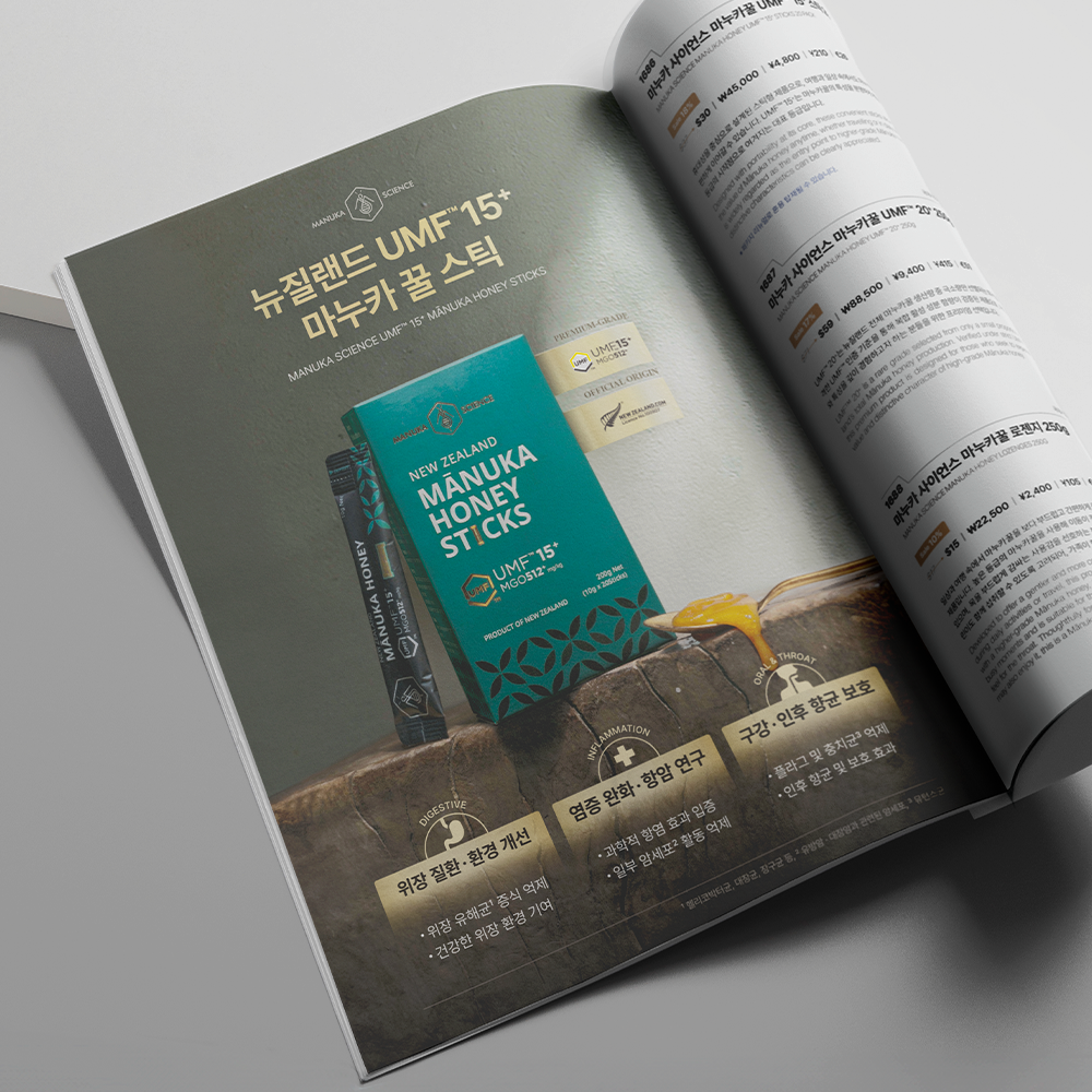 An open printed magazine or brochure spread on a light gray surface, showing a large advertisement for Manuka honey sticks. The left page features a teal and brown product box with Korean text, while the right page contains product information in English and Korean.