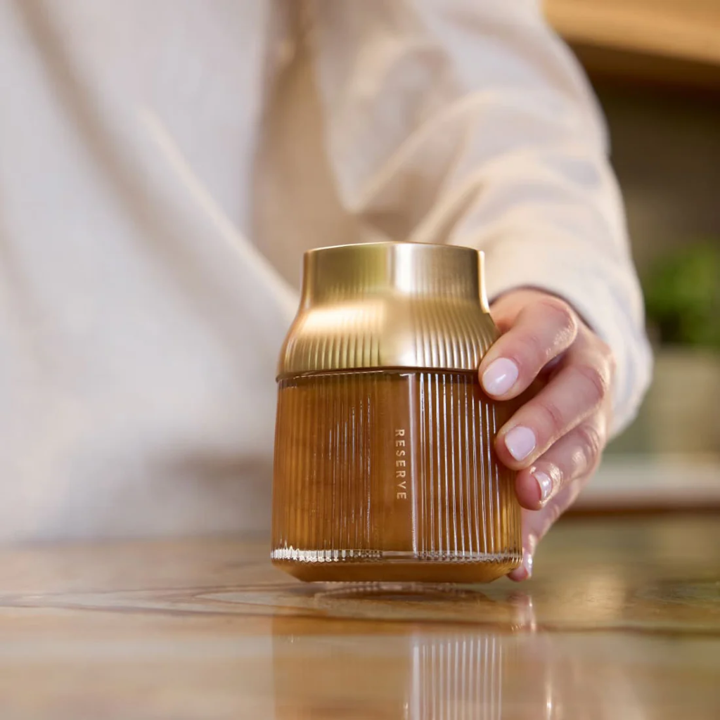Hand holding a gold and brown Manuka honey jar on a wooden surface