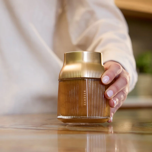 Hand holding a gold and brown Manuka honey jar on a wooden surface