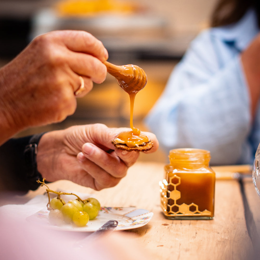 A honey dipper lifting from the jar, the honey falling slowly