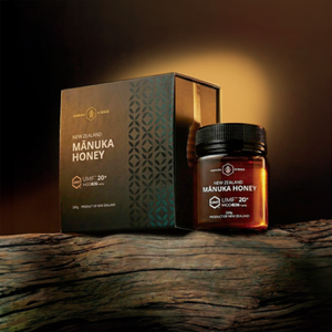 A jar of New Zealand Manuka Honey and its matching box are displayed on a rustic wooden surface against a dark, atmospheric background with a warm spotlight.