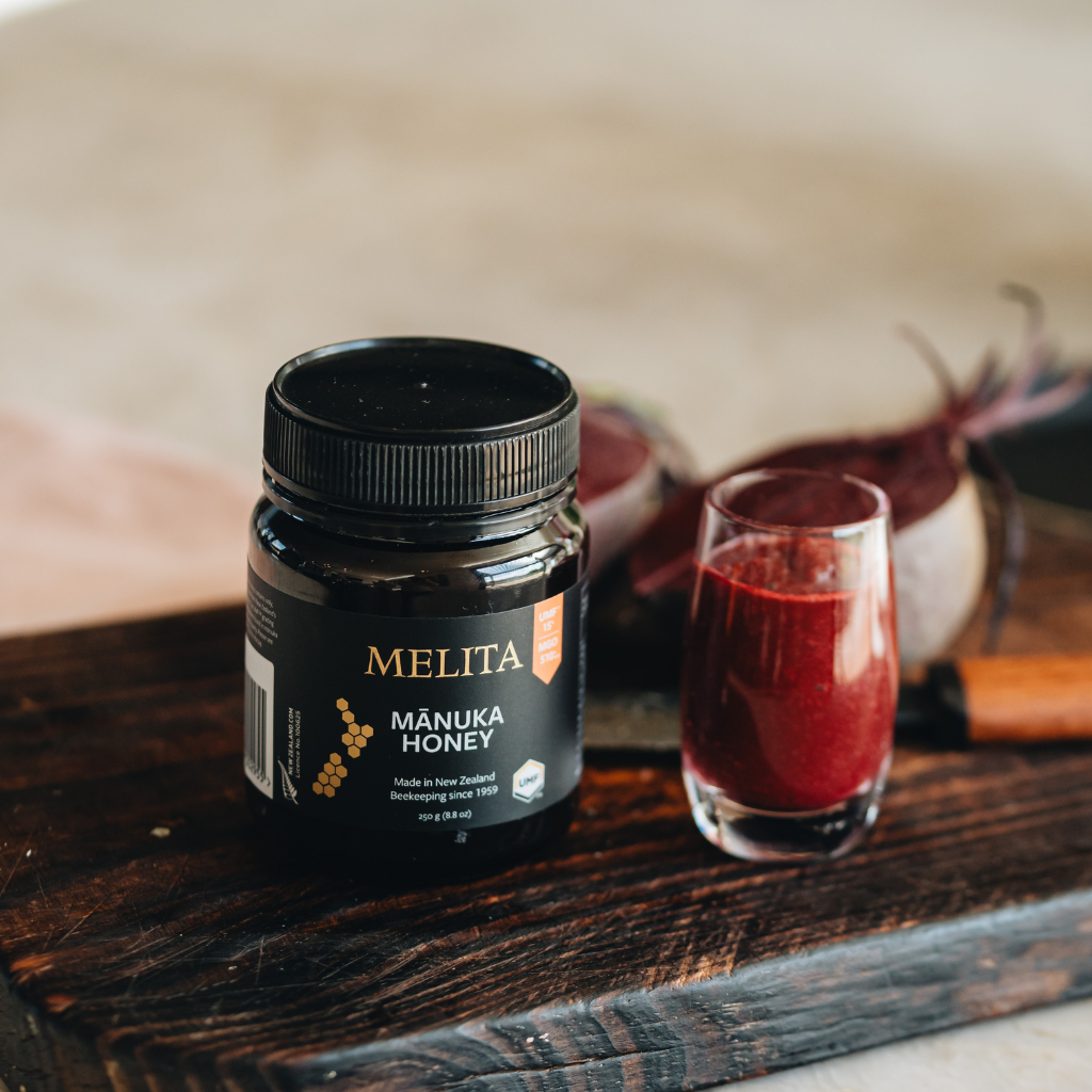 A jar of Melita Mânika Honey on a plain white background. The jar is black with a black ribbed lid, featuring gold and white text, a yellow honeycomb graphic, and an orange UMF badge.