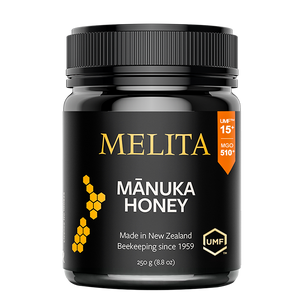 A jar of Melita Mânika Honey on a plain white background. The jar is black with a black ribbed lid, featuring gold and white text, a yellow honeycomb graphic, and an orange UMF badge.