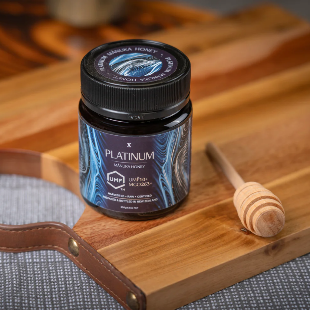 Jar of Platinum Manuka Honey on a wooden cutting board with a honey dipper.