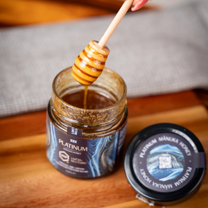 Jar of Platinum Manuka Honey with a honey dipper on a wooden surface