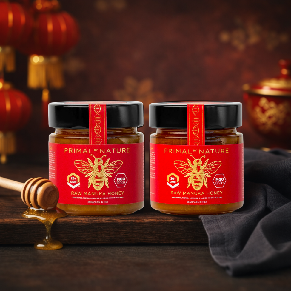 Two jars of Primal Nature raw manuka honey on a wooden surface with a honey dipper.