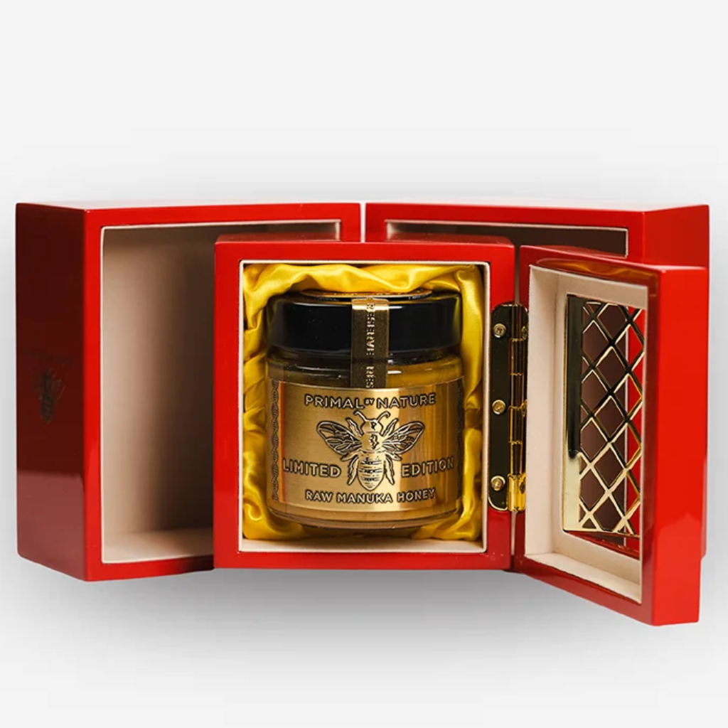 Primal by Nature 32+ UMF. A luxury jar of raw honey presented in an open red gift box with gold interior lining. 