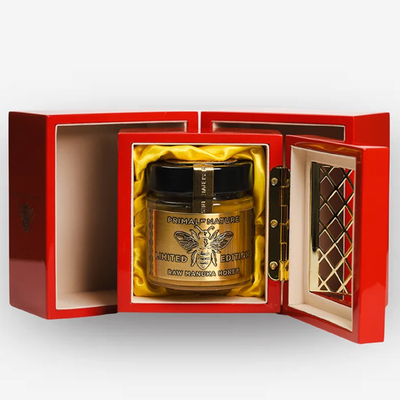 Primal by Nature 32+ UMF. A luxury jar of raw honey presented in an open red gift box with gold interior lining. 