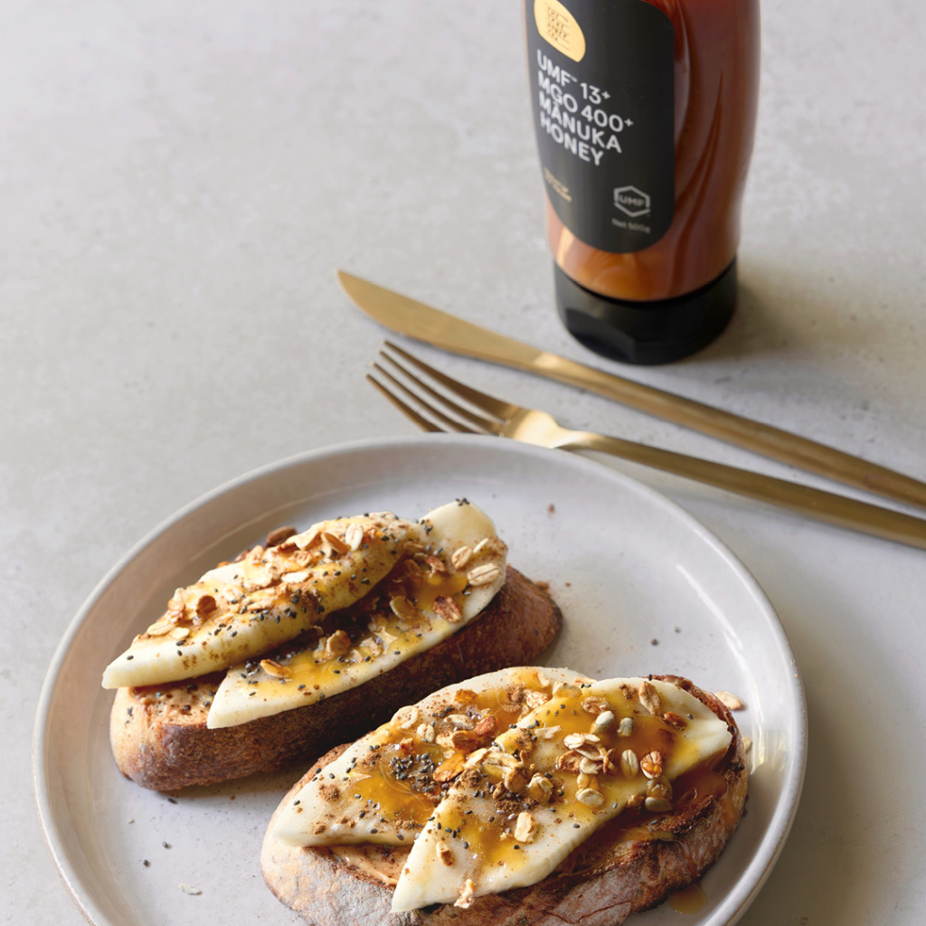 Two slices of toast with spread on a plate with a bottle of Manuka honey in the background.