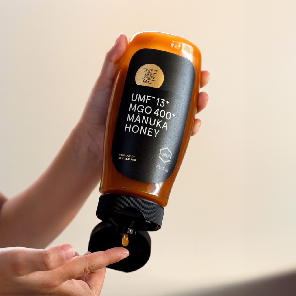 Hand holding a bottle of Manuka Honey with a beige background