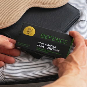 Person holding a box of DEFENCE 400+ Manuka Honey Lozenges with a sleep mask in the background.